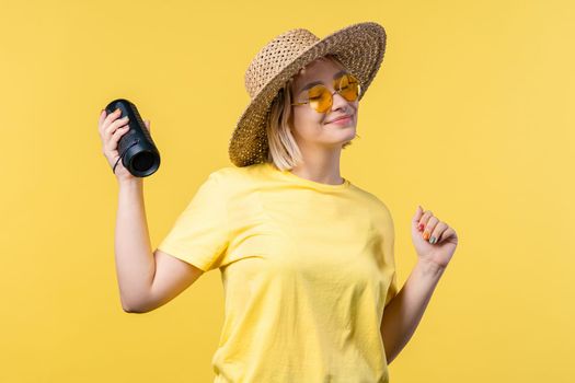 Lady dancing, enjoying on yellow studio background. She moves to rhythm of music. Young woman listening to music by wireless portable speaker - modern sound system.