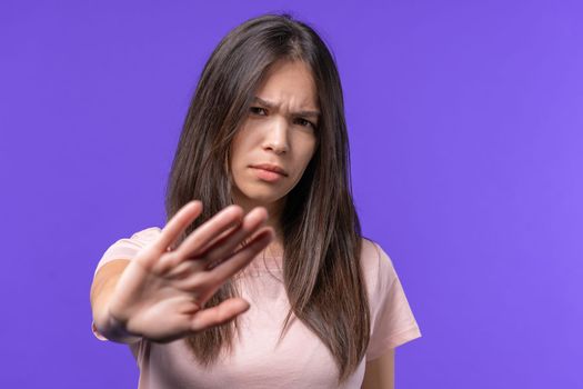 Uninterested teen girl disapproving with NO hand sign gesture. Denying, rejecting, disagree. Portrait of young woman on violet background, timeout concept.