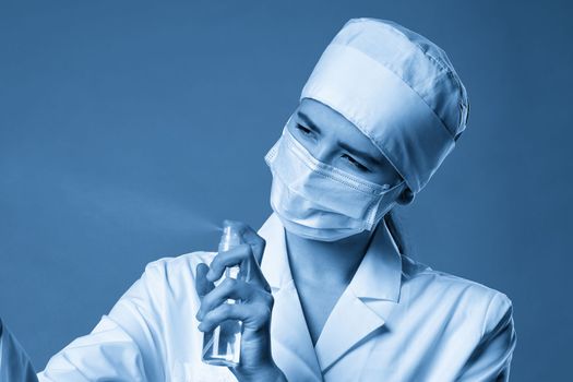 Young female doctor using spray antiseptic spray over blue background