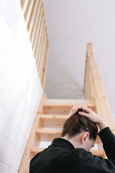 Young woman simple hairstyle back view by wooden stairs at home. Depression, loneliness and quarantine concept. Mental health, Self care, staying home.