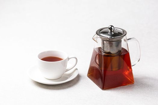Glass teapot with hot black tea with cup