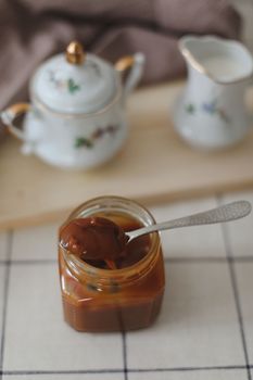 Homemade salted caramel sauce in jar on rustic wooden table.