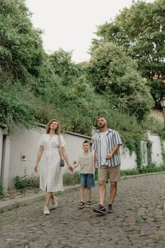 Father, mother and son are holding hands on the green cobbled street of an old European town. Happy family in the evening. Tourists at sunset.