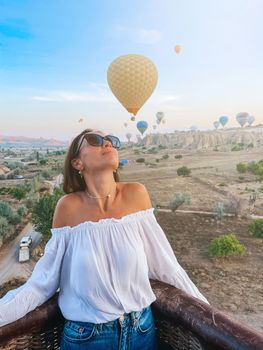 Happy woman during sunrise watching hot air balloons from a basket in the sky in Cappadocia, Turkey