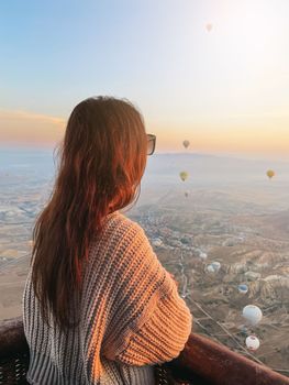 Happy woman during sunrise watching hot air balloons show from a basket in the sky in Cappadocia, Turkey
