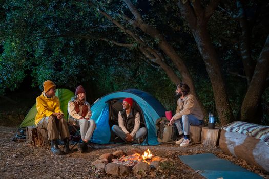 Group of multiethnic friends happy around the bonfire camping hike trekkers people having fun on excursion in the nature. Concept of community, youth lifestyle and friendship. High quality photo