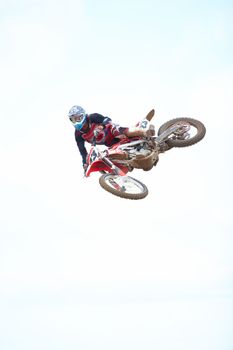 The definition of a daredevil. Low angle view of a motocross rider mid-air against a cloudy sky.