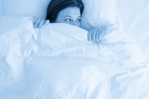 woman in bed looking surprised from under blanket