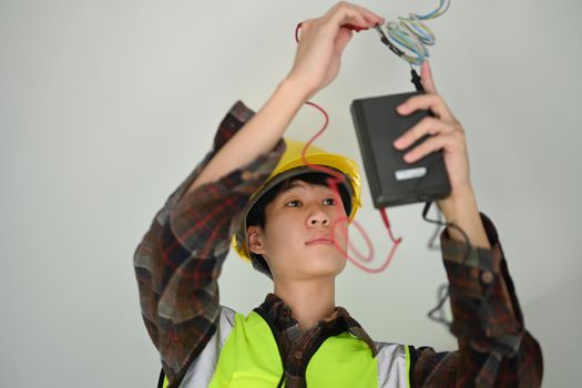 Asian male electrician using a multimeter measuring voltage and current of power electric line