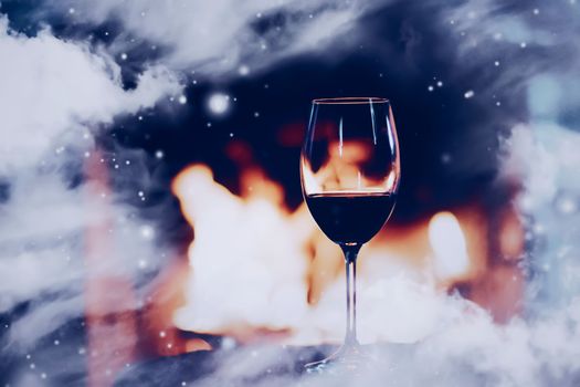 Winter atmosphere and Christmas holiday time, glass of wine in front of fireplace covered with snowy effect on window glass, holidays background