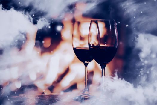 Winter atmosphere and Christmas holiday time, wine glasses in front of fireplace covered with snowy effect on window glass, holidays background