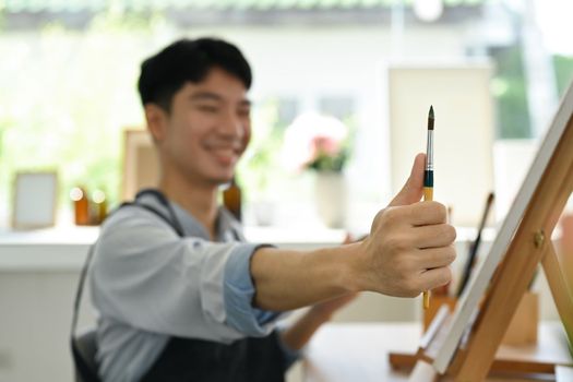 Image of pleased man artist painting picture with watercolor on canvas in art workshop. Art, creative hobby and leisure activity concept