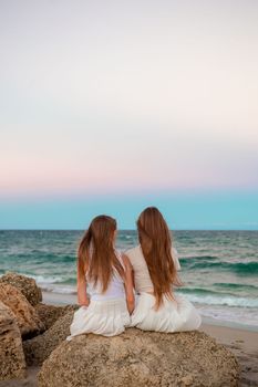 Adorable girls with long hair enjoy the view of the sea on the beach at sunset