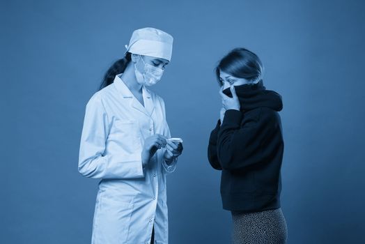 Young doctor measuring temperature of a patient with thermometer, studio shot on blue background