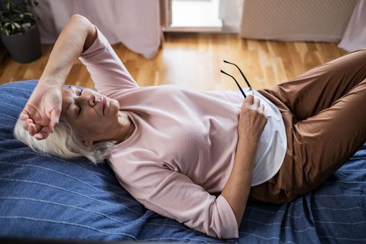 Senior woman suffering from a headache resting at home on sofa