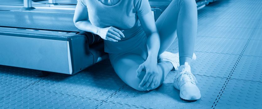 Young woman in sportswear having pain in her knee while training in gym, Girl sitting on a floor touching her knee in pain