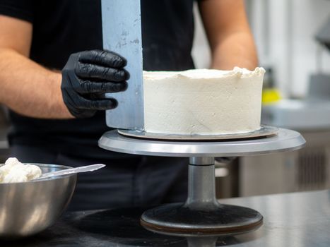 chef smoothing a forsted cake with buttercream, spatula and wrench