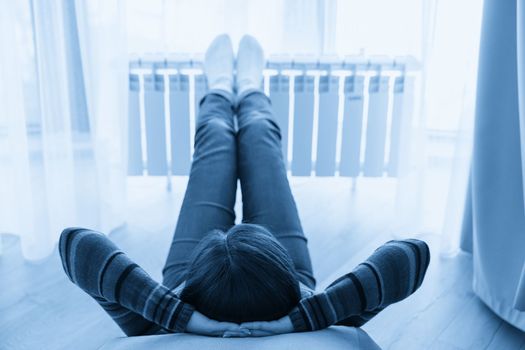 Woman laying on floor with feet raised up on radiator for warming up