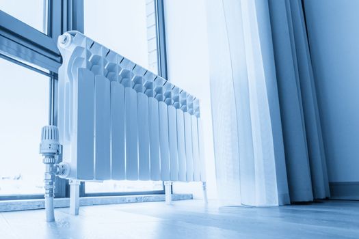 White big radiator near window in modern room, sepia toning