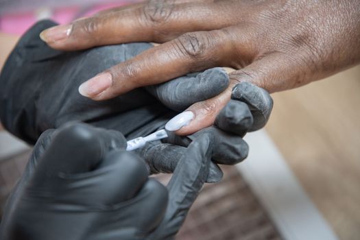 Manicurist covers the nails of a dark-skinned girl with blue gel polish 