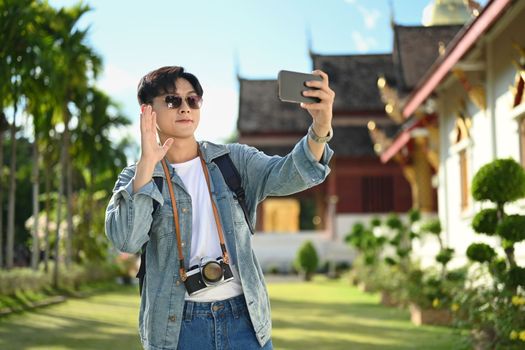 Male traveller making photos for social media on with scenery view of buddhist temple pagoda in background