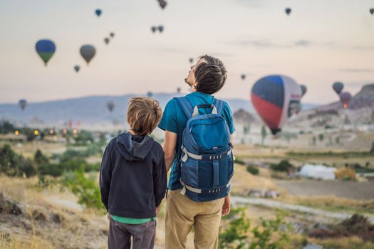 Tourists father and son looking at hot air balloons in Cappadocia, Turkey. Happy Travel in Turkey concept. father and son on a mountain top enjoying wonderful view.