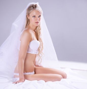 Femininity is key for your wedding day. a beautiful young bride sitting on a bed in lingerie.