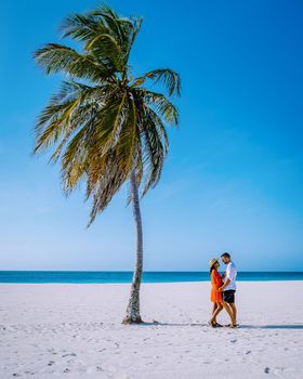 Couple men and women wit a Palm Trees on the shoreline of Eagle Beach in Aruba