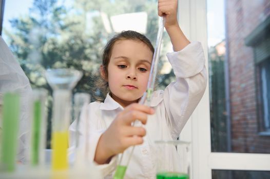 Smart primary school student using pipette, drips reagent into a test tube while chemical experiments at chemistry class
