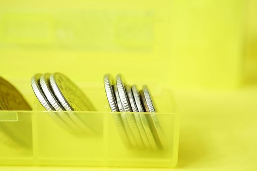 close up of coins in a plastic box on yellow background 