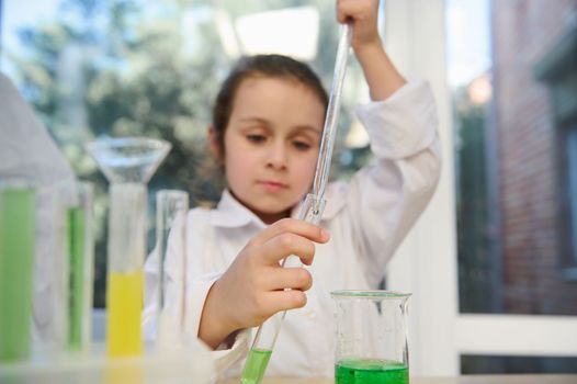 Focus on graduated pipette with several drops of reagent, in hands of school girl drips a liquid chemical into test tube