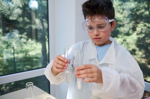 Teen schoolboy wearing white lab coat, holding test tubes with chemicals chemistry laboratory. Kids and science concept
