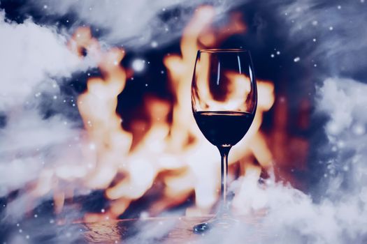 Winter atmosphere and Christmas holiday time, glass of wine in front of fireplace covered with snowy effect on window glass, holidays background
