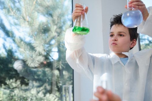 Inspired young chemist, smart nerd schoolboy examining solutions in the lab flasks in the school laboratory. Copy space