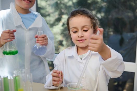 Beautiful smiling little school girl enjoying chemistry class in school laboratory. Kids conducting chemical experiments