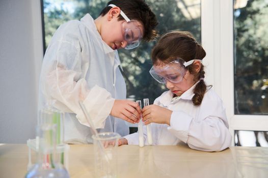 Concentrated smart kids conduct chemical experiment, watch the reaction taking place in test tubes at chemistry class