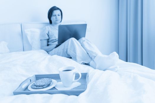 Woman in bed with laptop and breakfast