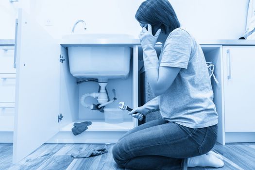Woman sitting near leaking sink in laundry room calling for help