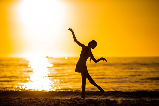 Silhouette of the beautiful girl dancing on the beach at sunset