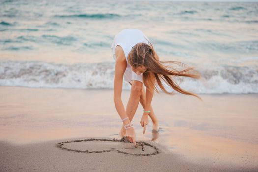 Cute teen girl with long hair have fun on the beach and drawing on the sand
