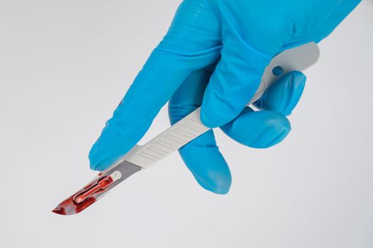Female hand in a glove with a bloody scalpel on a white background.