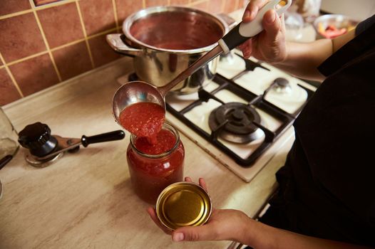 Top view of a housewife pouring freshly boiled tomato juice into a sterilized jar, preparing homemade organic passata
