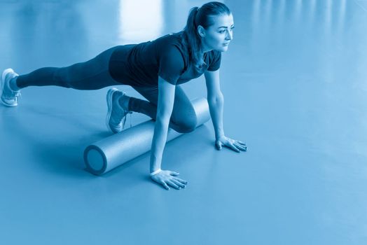Attractive female exercising pilates fitness doing foam roller exercise and posing in modern bright fitness center