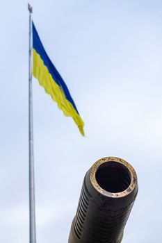 Groups of ancient military guns against the background of the State Flag of Ukraine. Muzzle brake of an artillery gun. Sunny morning sky. Call to stop violence concept. Ukrainian flag.