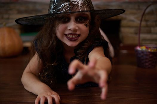 A little witch in sorcerer's hat reaches out her hand, looking at the camera with a frightening look. Halloween concept