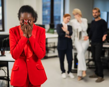 Young african woman crying because of the ridicule of colleagues. Racial discrimination in the office.