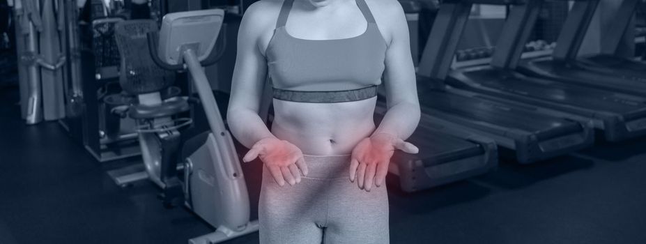 Young woman in sportswear having ache on palms after training in gym