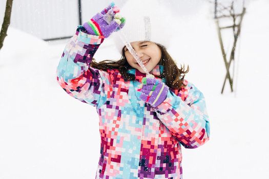 Cute child girl holding icicle. Winter portrait of little caucasian child girl wearing hat and hold big icicle. Outdoor winter activities for kids