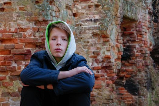 Teenager sits on the ground near a brick house. 