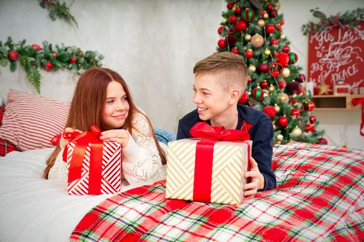 A cheerful teenagers opens a Christmas gifts. Cheerful Teenagers lies in bed with a christmas presents in they hands